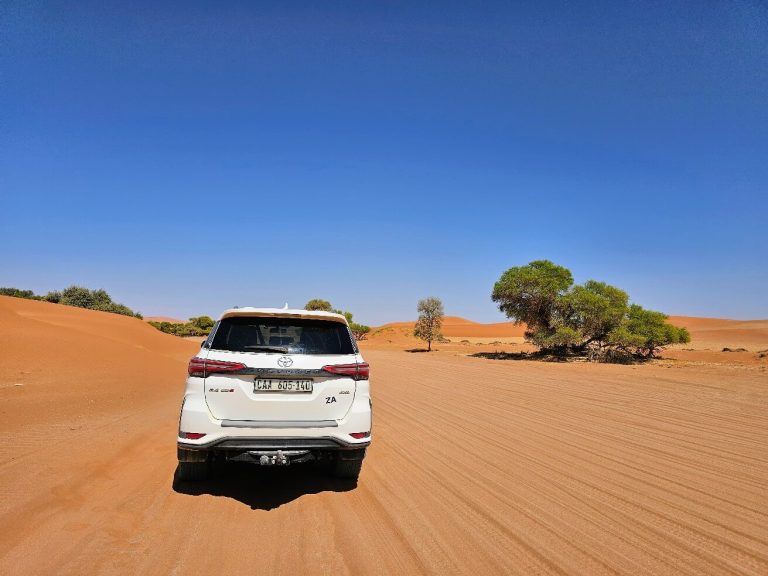 White 4x4 on a red sand track past camelthorn trees