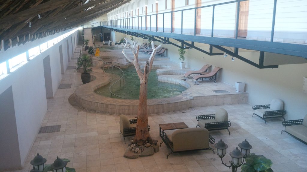 The indoor thermal pool at Ai-Ais, a green-tiled spring-fed pool with loungers beneath a thatched and glazed roof