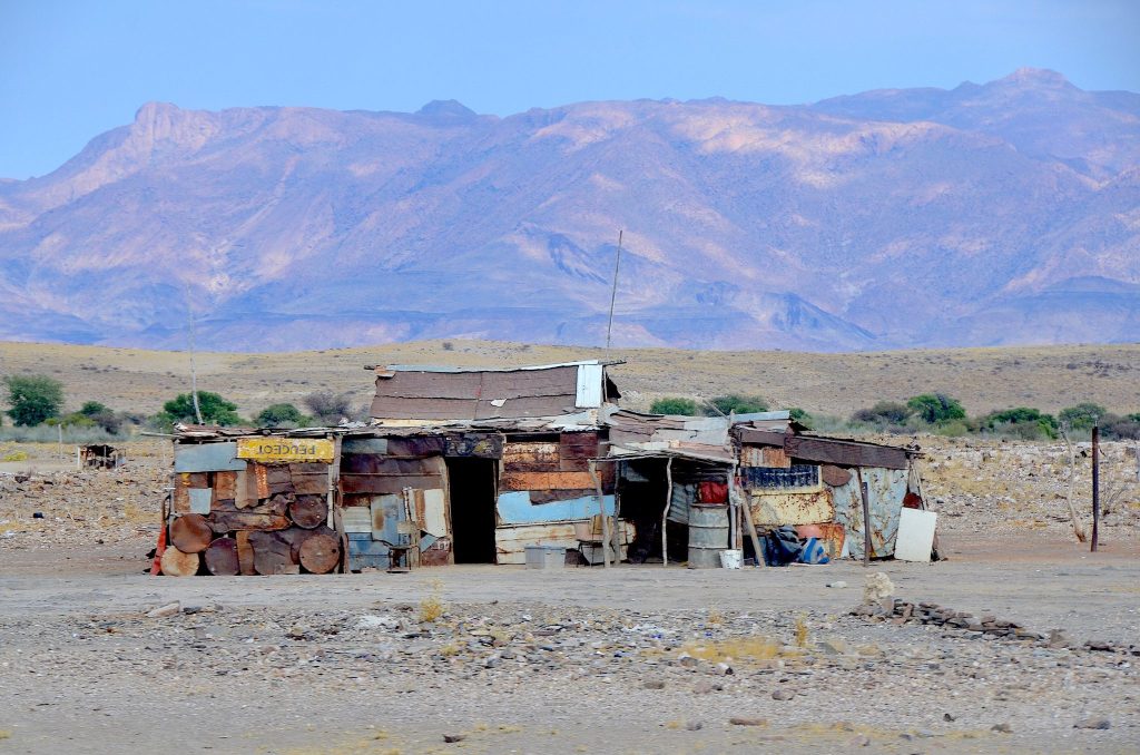 A shack built from corrugated iron sheets and oil drums standing alone on the stony plain near Uis, with the long purple ridge of the Brandberg massif rising behind