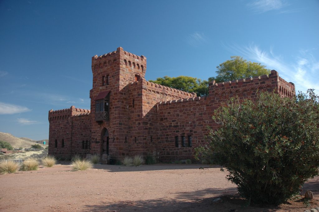 Duwisib Castle, a red sandstone fort with crenellated walls and a square tower, standing on bare desert ground