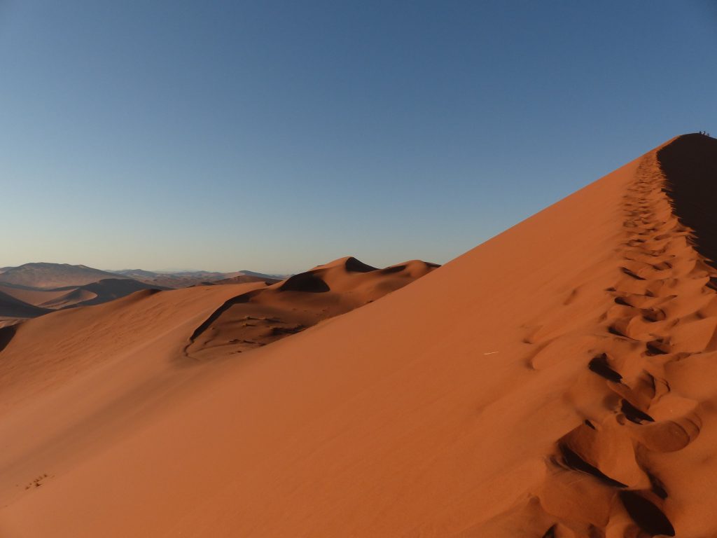 Footprints along dune ridge with distant mountains, Namibia