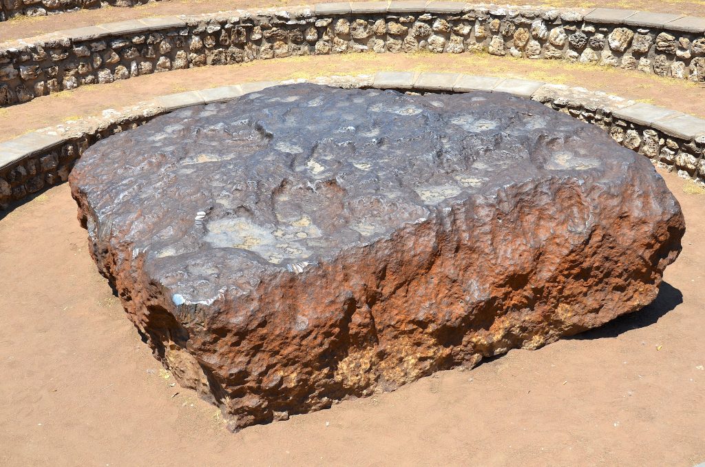 The rust-brown iron slab of the Hoba meteorite lying in its circular stone-walled amphitheatre near Grootfontein