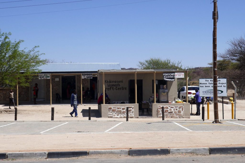 A row of small roadside businesses in Kamanjab including a beauty salon, barber shop and the Khaimaseni Women's Craft Centre under a corrugated iron verandah