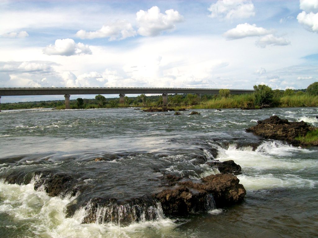 The long concrete road bridge at Katima Mulilo spanning the Zambezi River, with water breaking white over dark rock ledges in the foreground