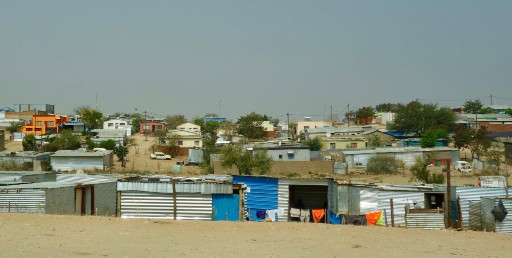 A wide view across Katutura township on the edge of Windhoek, with rows of corrugated-iron homes in the foreground and painted brick houses spread over the rise behind