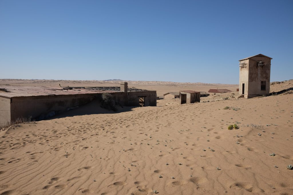 Sand drifting through the roofless ruins of Kolmanskop ghost town, with a tall two-storey building standing alone on the dune