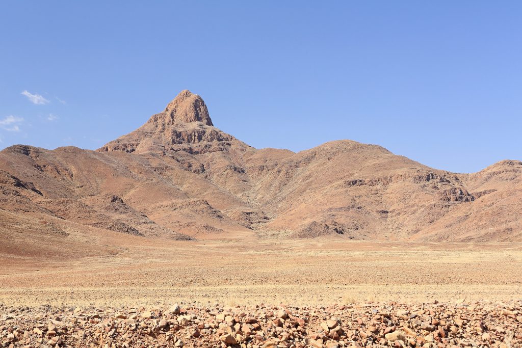 A pointed rust-coloured peak rising above a stony gravel plain in the NamibRand Nature Reserve