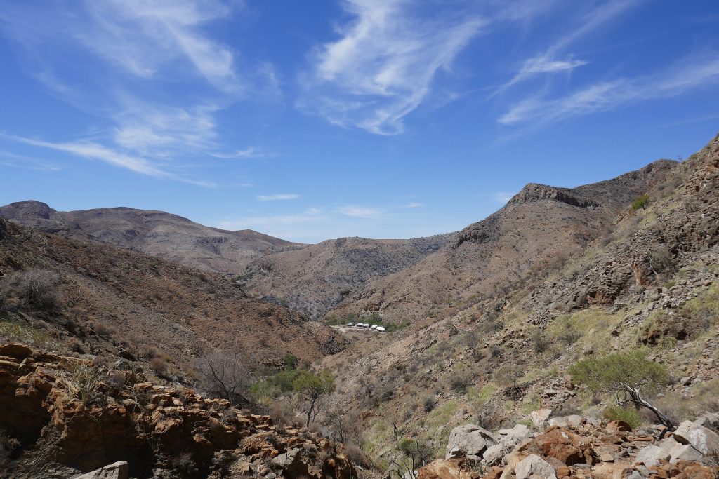 A dry rocky valley winding between the arid slopes of the Naukluft Mountains under wispy high cloud