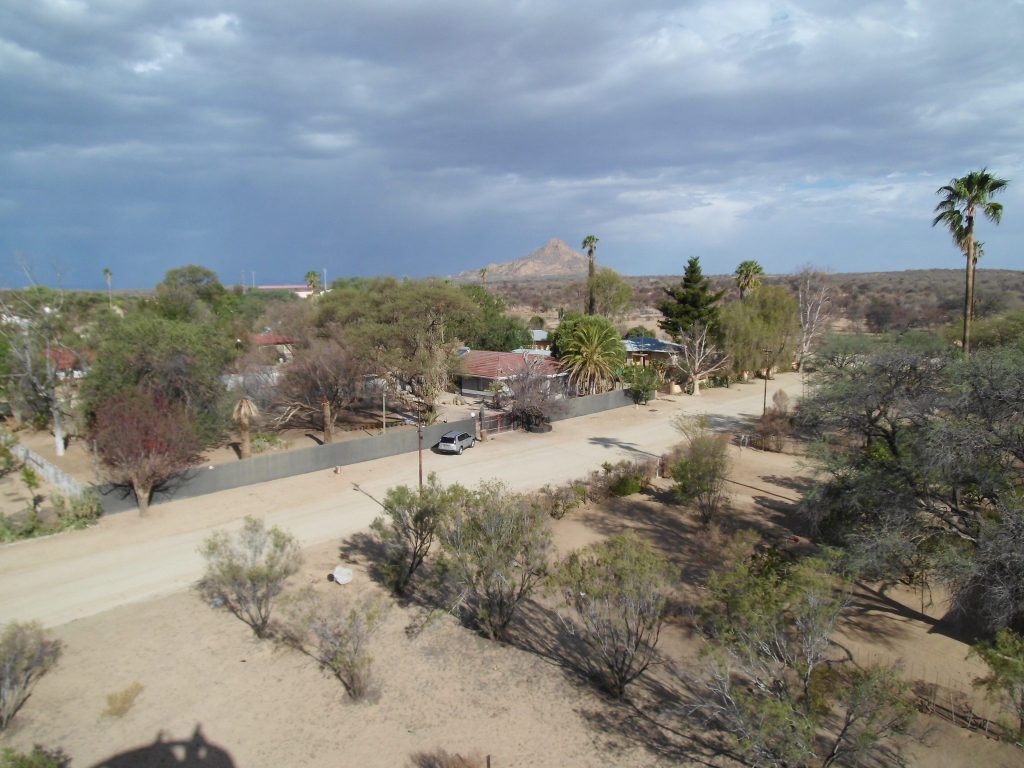 View from the Franke Tower over the tin roofs, palms and sandy streets of Omaruru, with a pointed rocky peak on the horizon under storm clouds