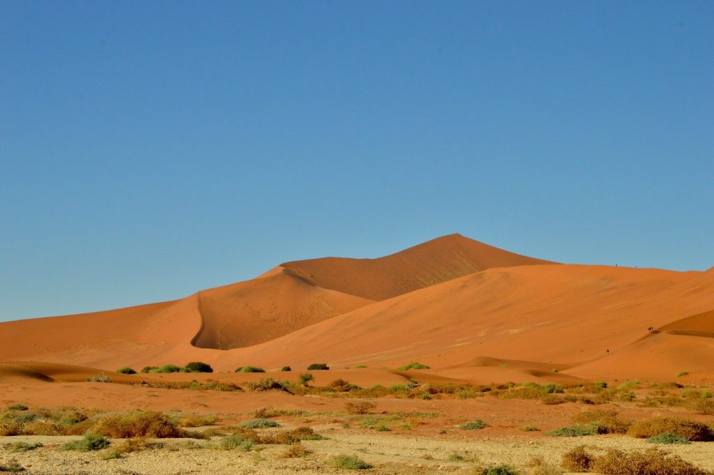 Red dune peak under cloudless sky above gravel plain, Namibia