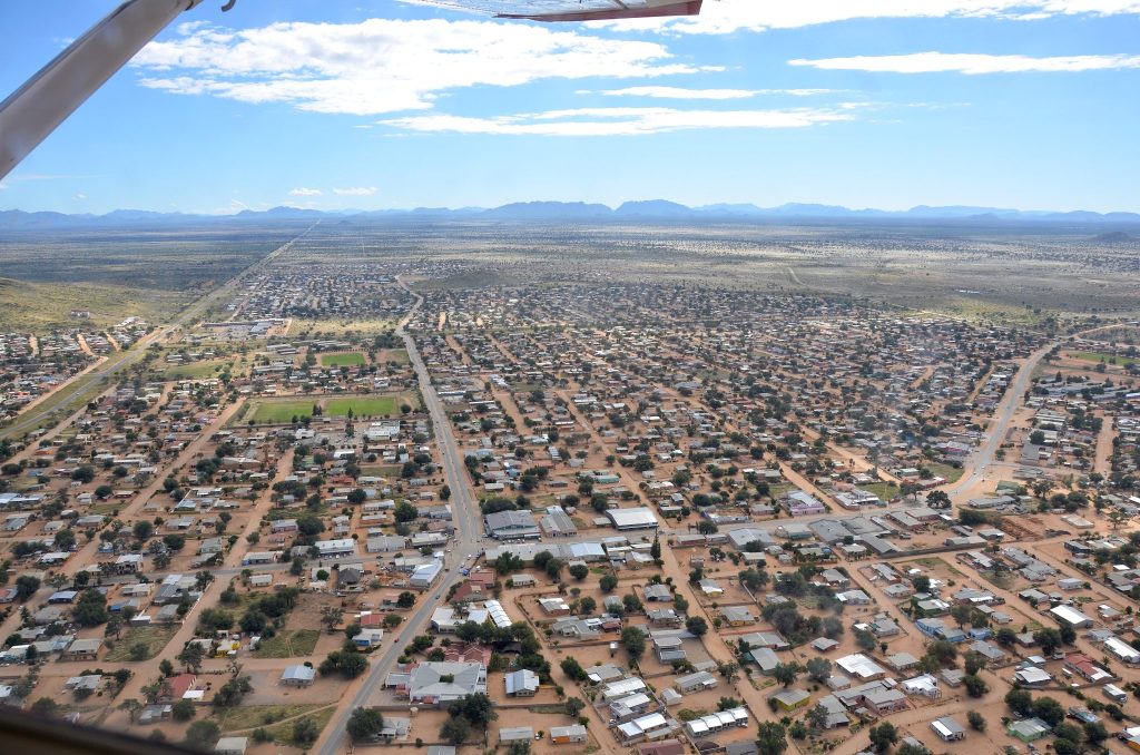 Aerial view over Rehoboth showing the tarred main road running through a wide grid of sandy streets and low houses, with hills on the far horizon
