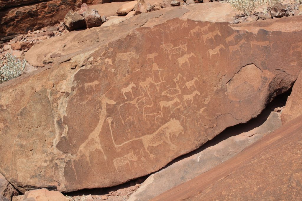 A tilted sandstone slab at Twyfelfontein covered in prehistoric engravings of giraffe, antelope and other animals