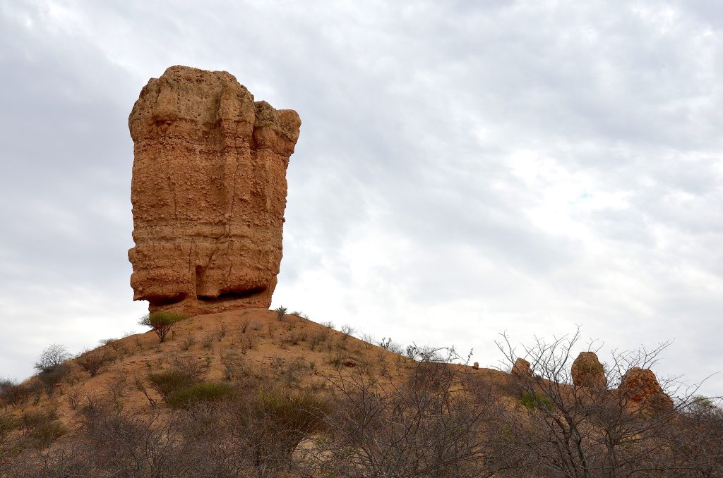 The Vingerklip, a tall isolated finger of layered rock standing on a low hill above dry thornbush in the Ugab Valley
