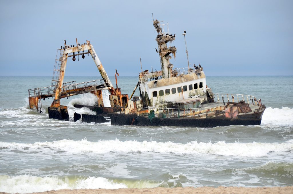 The rusting hull of the fishing trawler Zeila listing in the breakers off the Skeleton Coast, cormorants perched on its masts